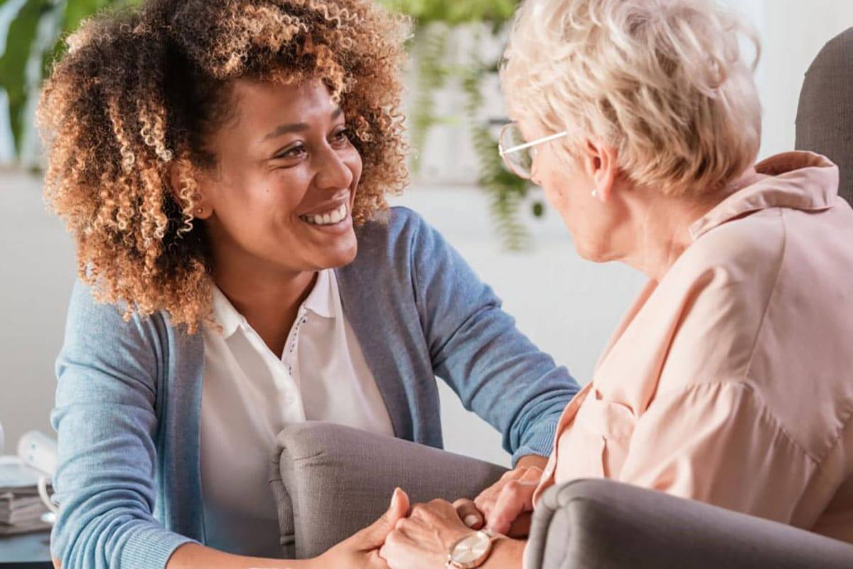 A Woman Talking To An Older Woman In A Chair.